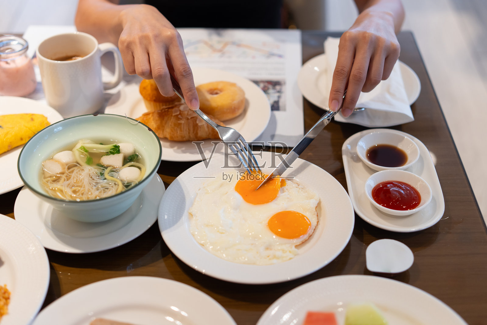 女人的手用餐具切开煎蛋的蛋黄。照片摄影图片