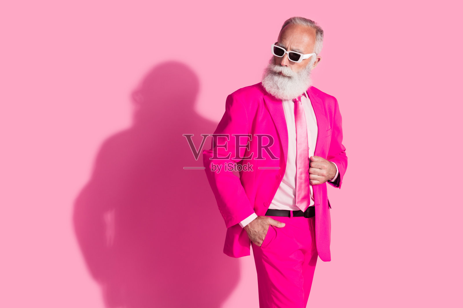 自信的酷炫退休圣诞老人男主播，穿着粉色西装，戴着太阳镜，背景为空白的柔和色调。照片摄影图片