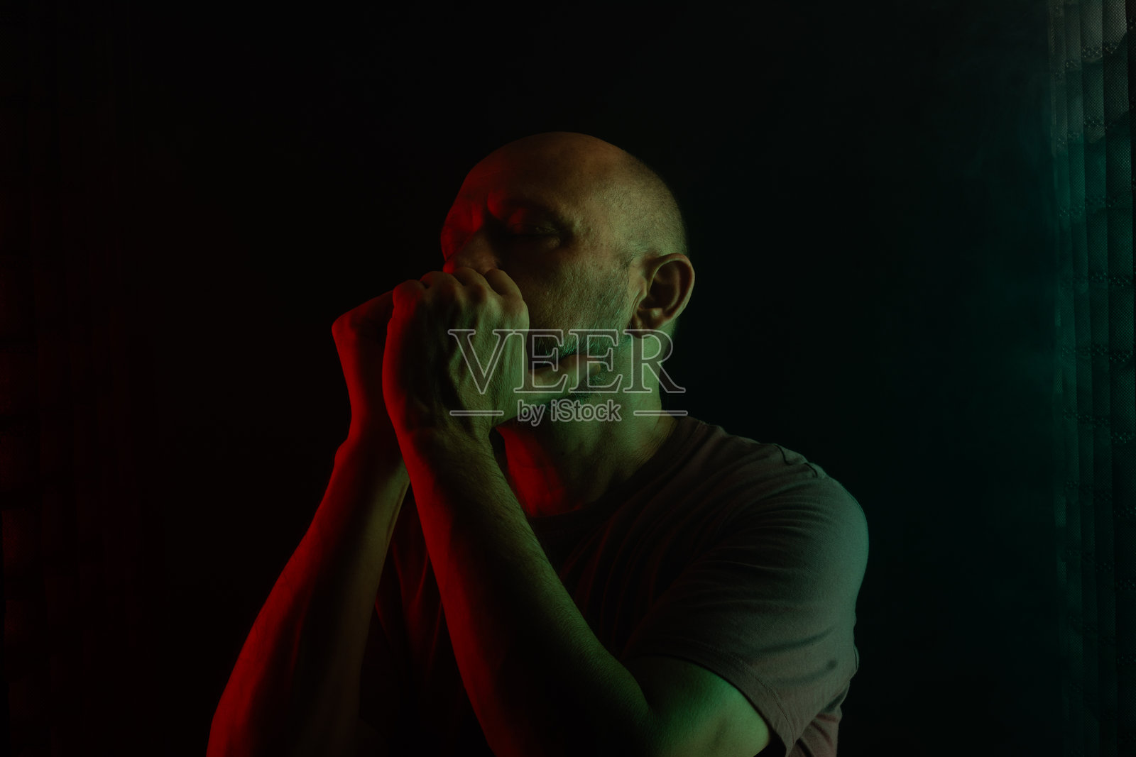 光头胡子男人用手做出绝望的手势。背景为烟雾弥漫的黑色，配有彩色灯光。照片摄影图片