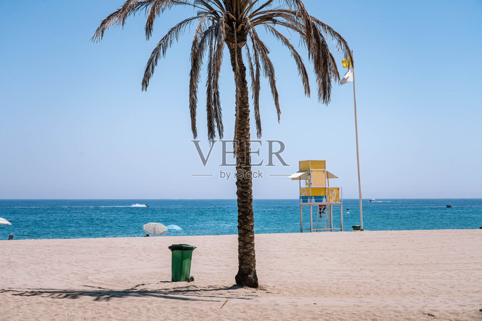 美丽的夏日沙滩，棕榈树、救生塔和垃圾桶相伴照片摄影图片
