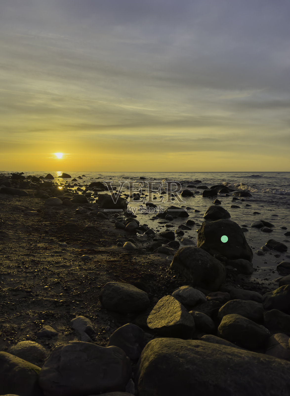 巴尔蒂克海鲁根岛的海滩日落，水中有大石头，竖版。照片摄影图片