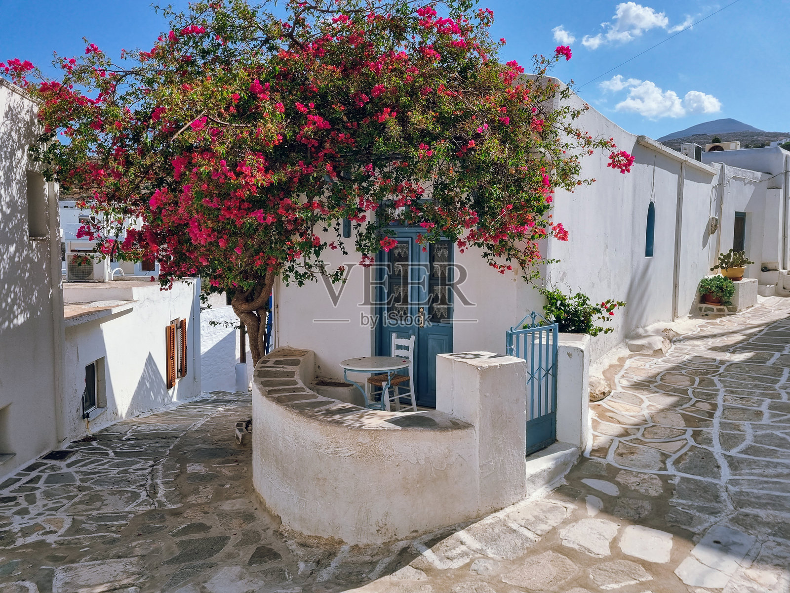 迷人的传统希腊房屋，位于角落，有小阳台，蓝色的门窗和粉色的花朵（九重葛），位于希腊帕罗斯岛的莱夫基斯村。照片摄影图片