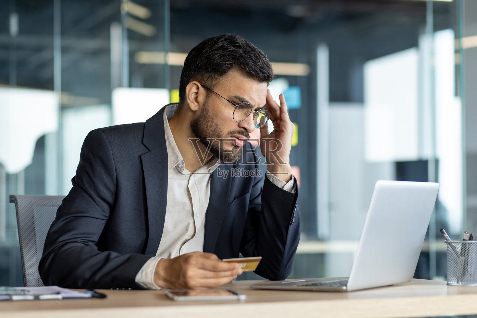 压力大的商人在办公室使用笔记本电脑时握着信用卡照片摄影图片