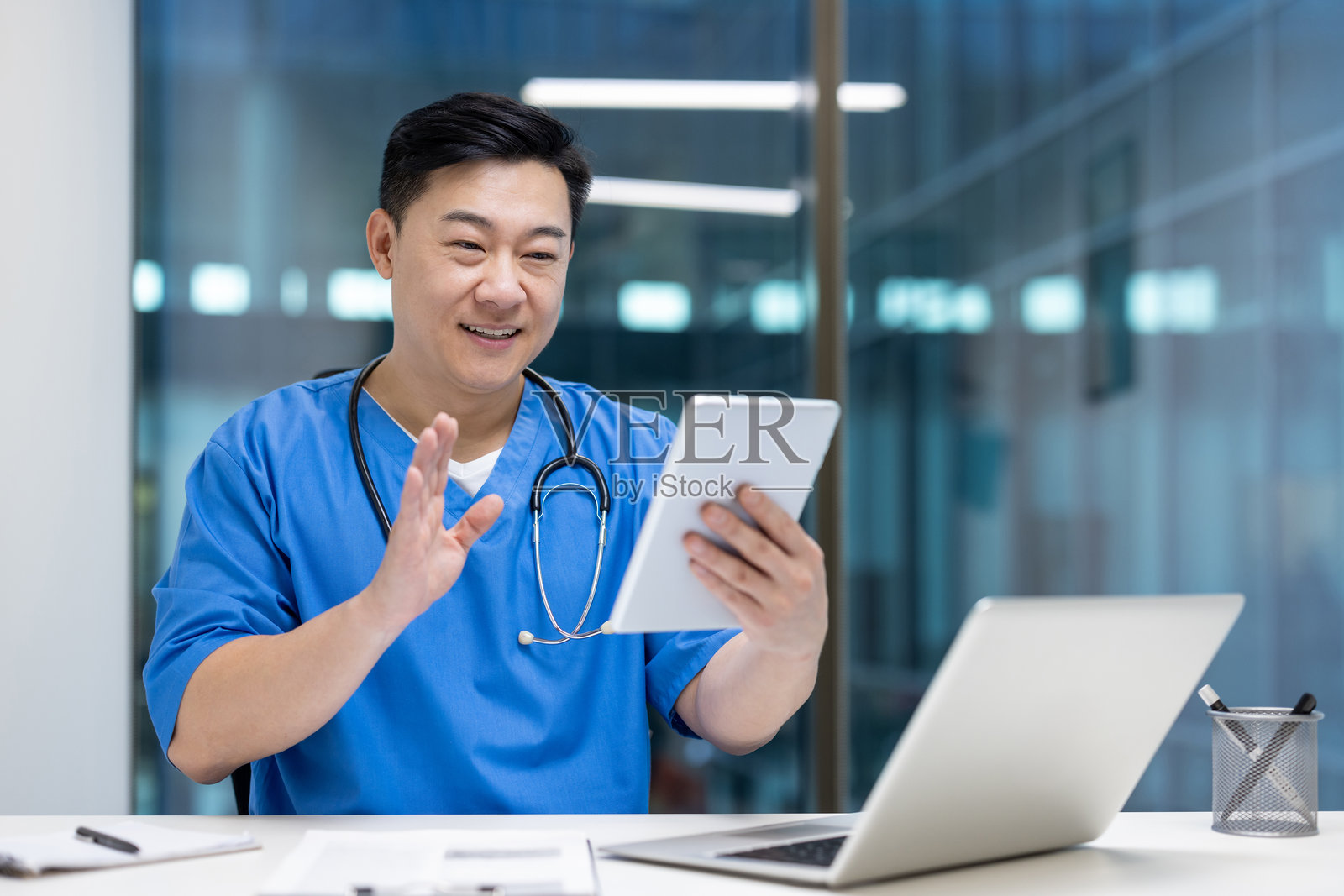 亚洲男性医生在现代办公室环境中自信地微笑着使用平板进行虚拟咨询照片摄影图片