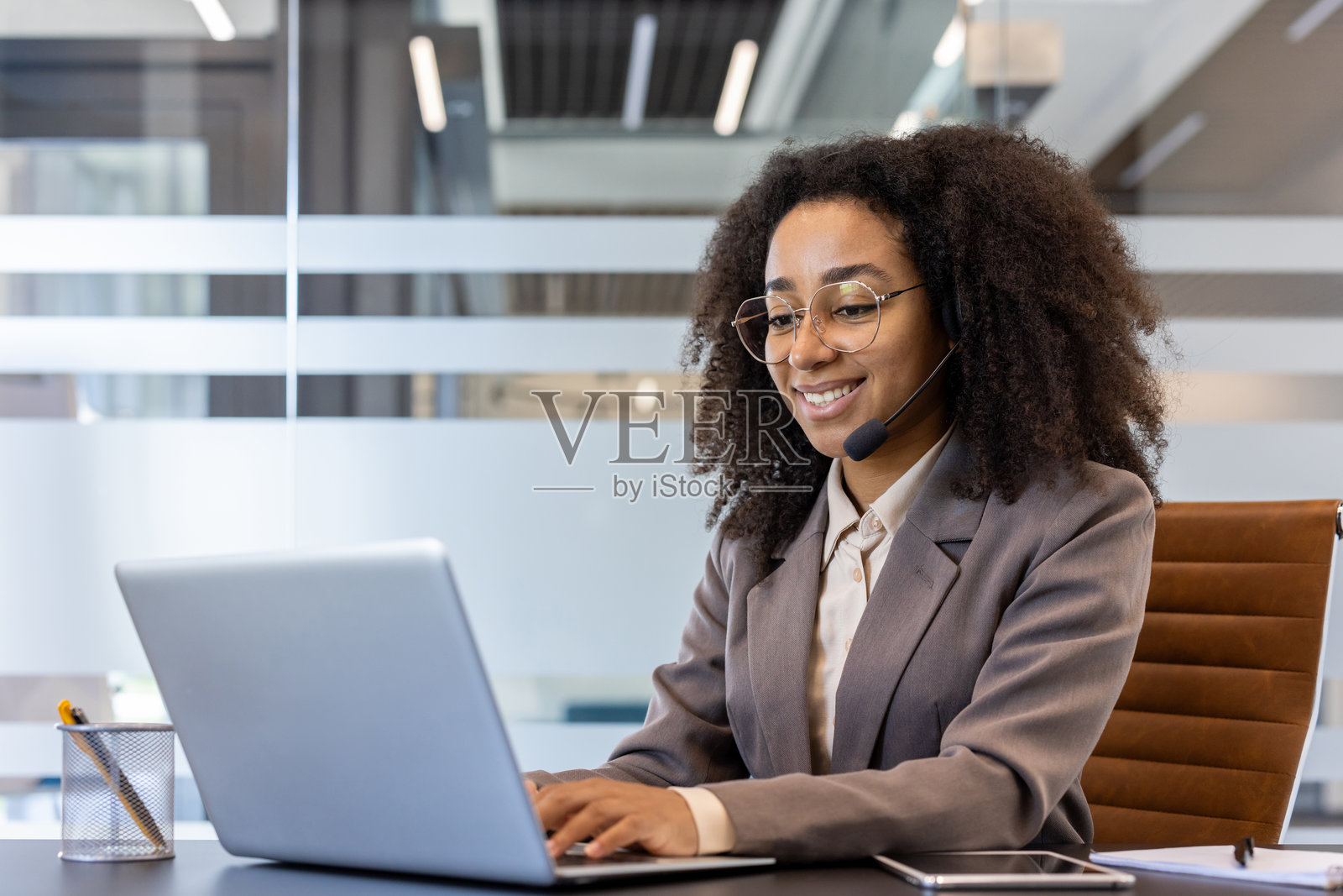 微笑的年轻非裔美国女商人在办公室的桌子前穿着西装，使用笔记本电脑工作照片摄影图片