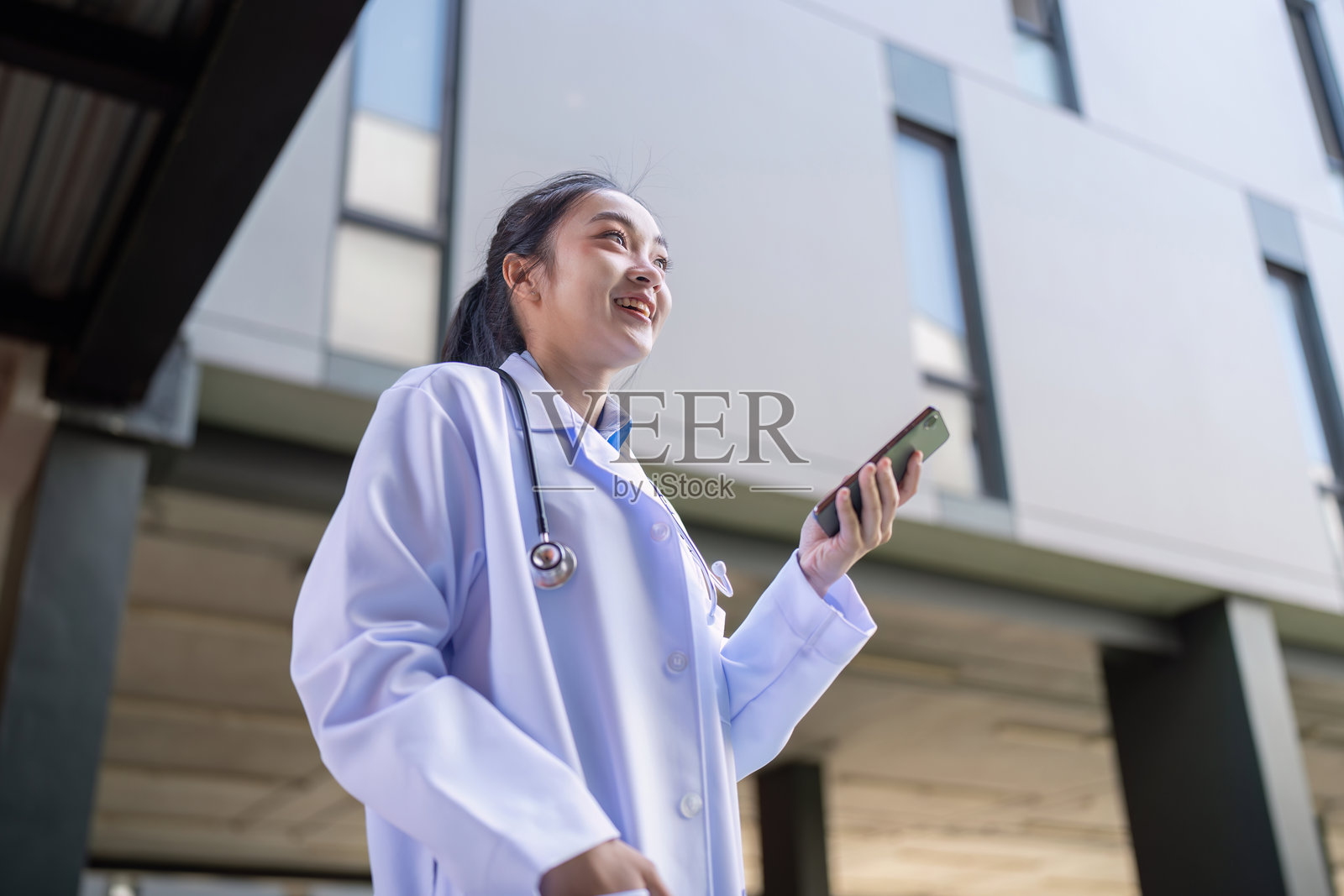 户外微笑的亚洲女性医生手持智能手机照片摄影图片