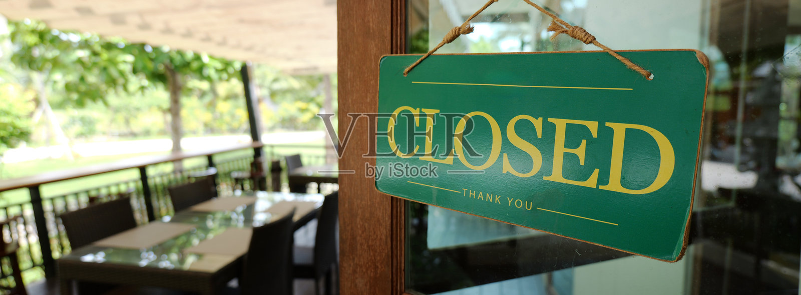 一家餐厅的门前挂着关闭的标志，周围有户外座位和绿色环境。照片摄影图片