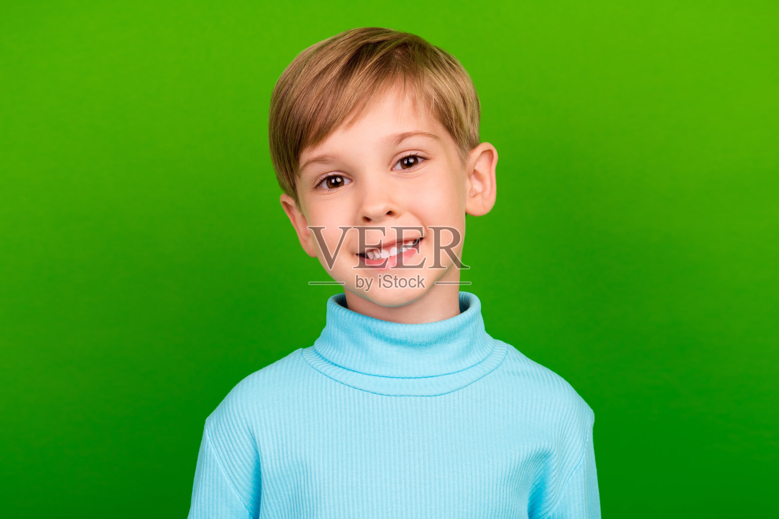 可爱的甜美小男孩穿着青绿色高领毛衣，微笑着，背景为绿色。照片摄影图片