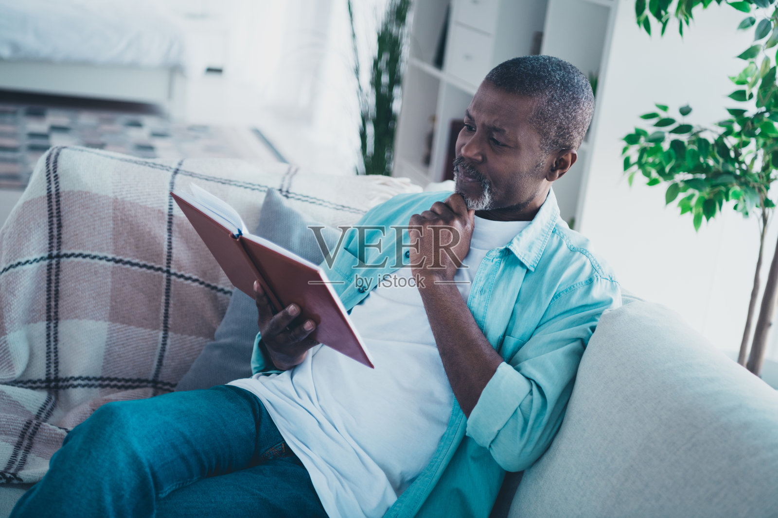 一位思维敏捷的中年男子坐在舒适的沙发上，阅读有趣的百科全书，思考创意，身处现代客厅。照片摄影图片