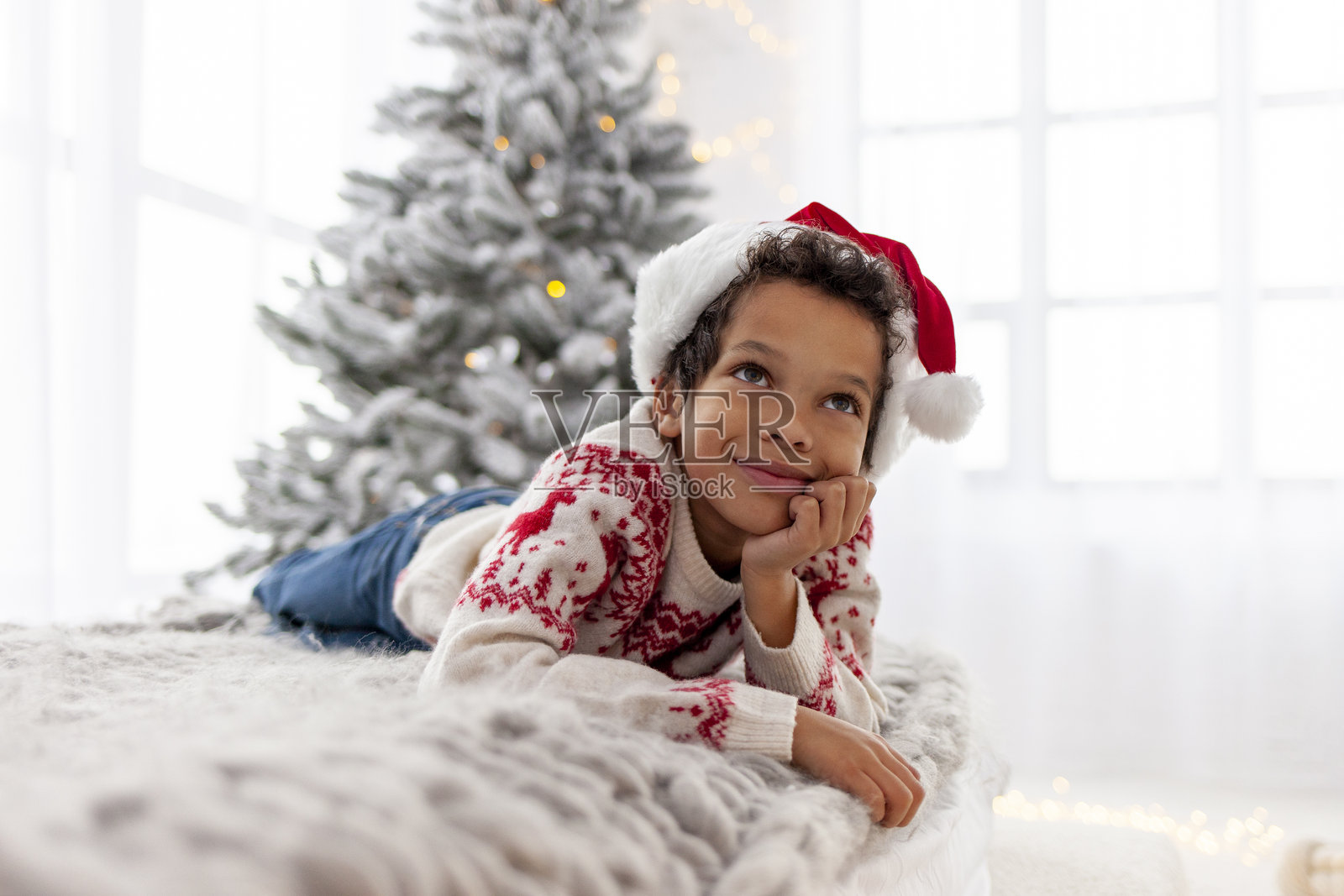 身穿圣诞毛衣和圣诞帽的非裔美国少年躺在家里的床上做梦照片摄影图片