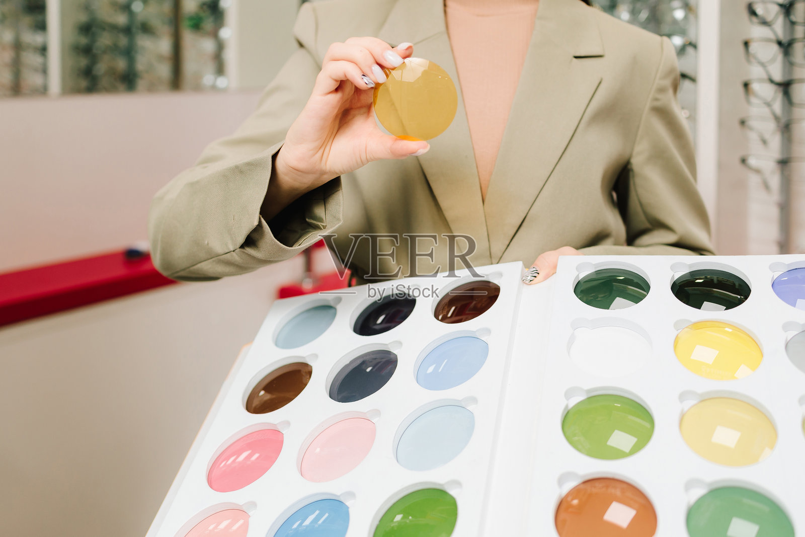 女性顾客在眼镜店里拿着五彩缤纷的光学镜片。验光后选择眼镜镜片。丰富多样的彩色镜片供视力矫正使用。照片摄影图片