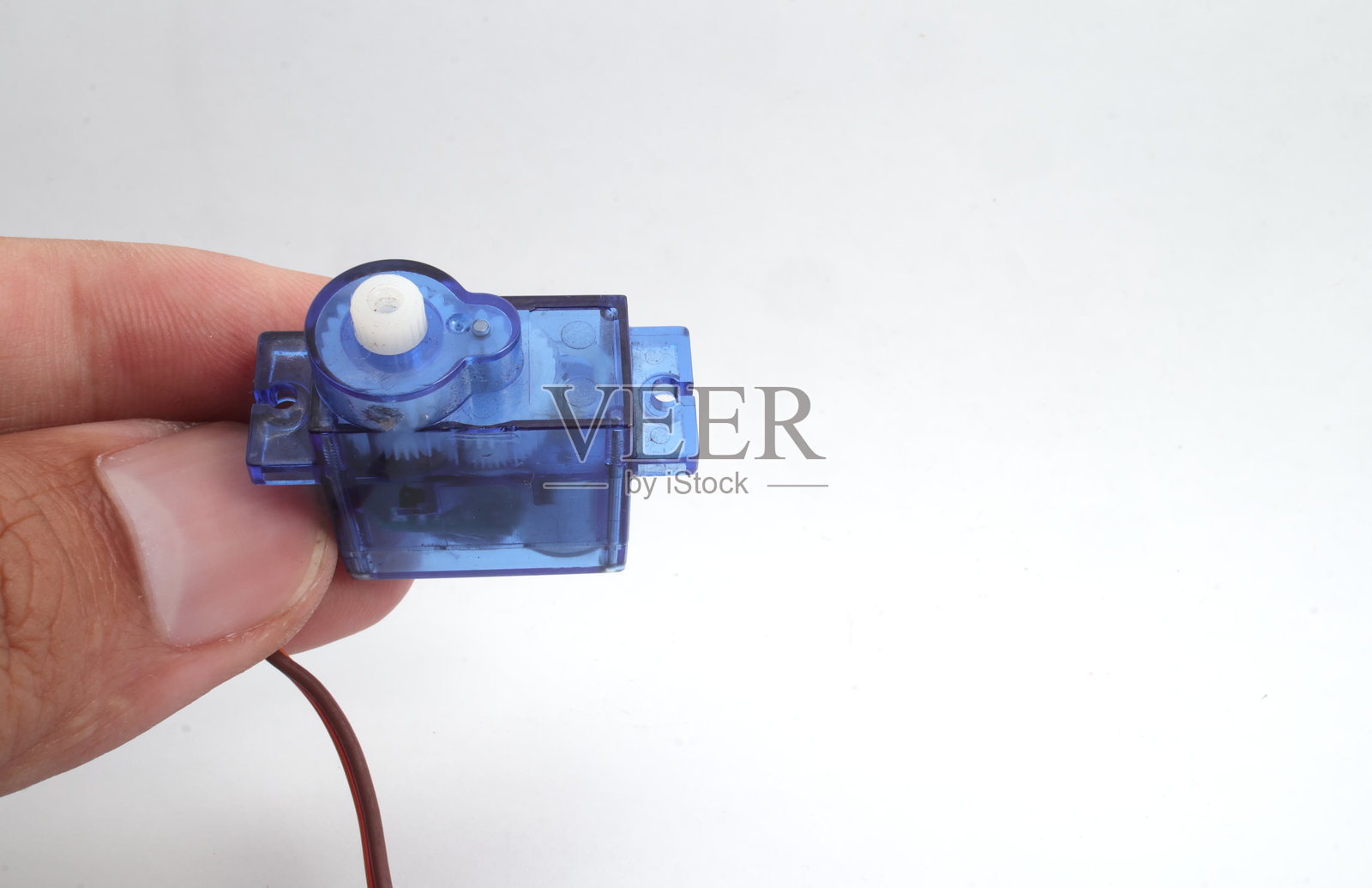一只蓝色塑料微型伺服电机被手握住，背景为白色。这是一种电气设备，可以以非常精确的控制角度位置、加速度和速度来推动或旋转物体。广泛应用于电子、机电一体化、机器人和遥控设备。照片摄影图片