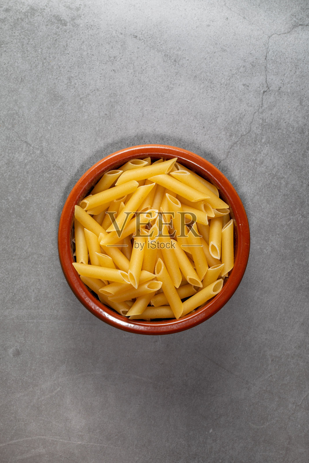 从上方拍摄的厨房工作台上的陶土碗，盛满了通心粉（笔形通心粉）。照片摄影图片