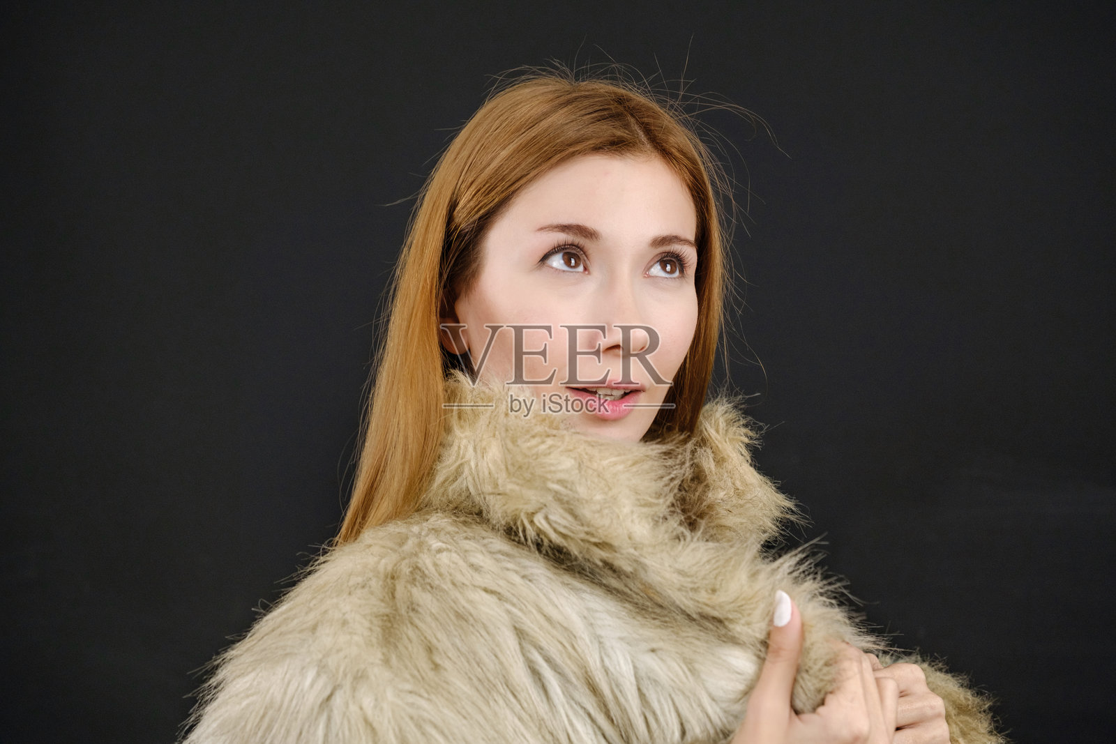 一位年轻女性的头像肖像，棕色头发，穿着米色毛皮外套，拍摄于黑色背景的摄影棚中。照片摄影图片