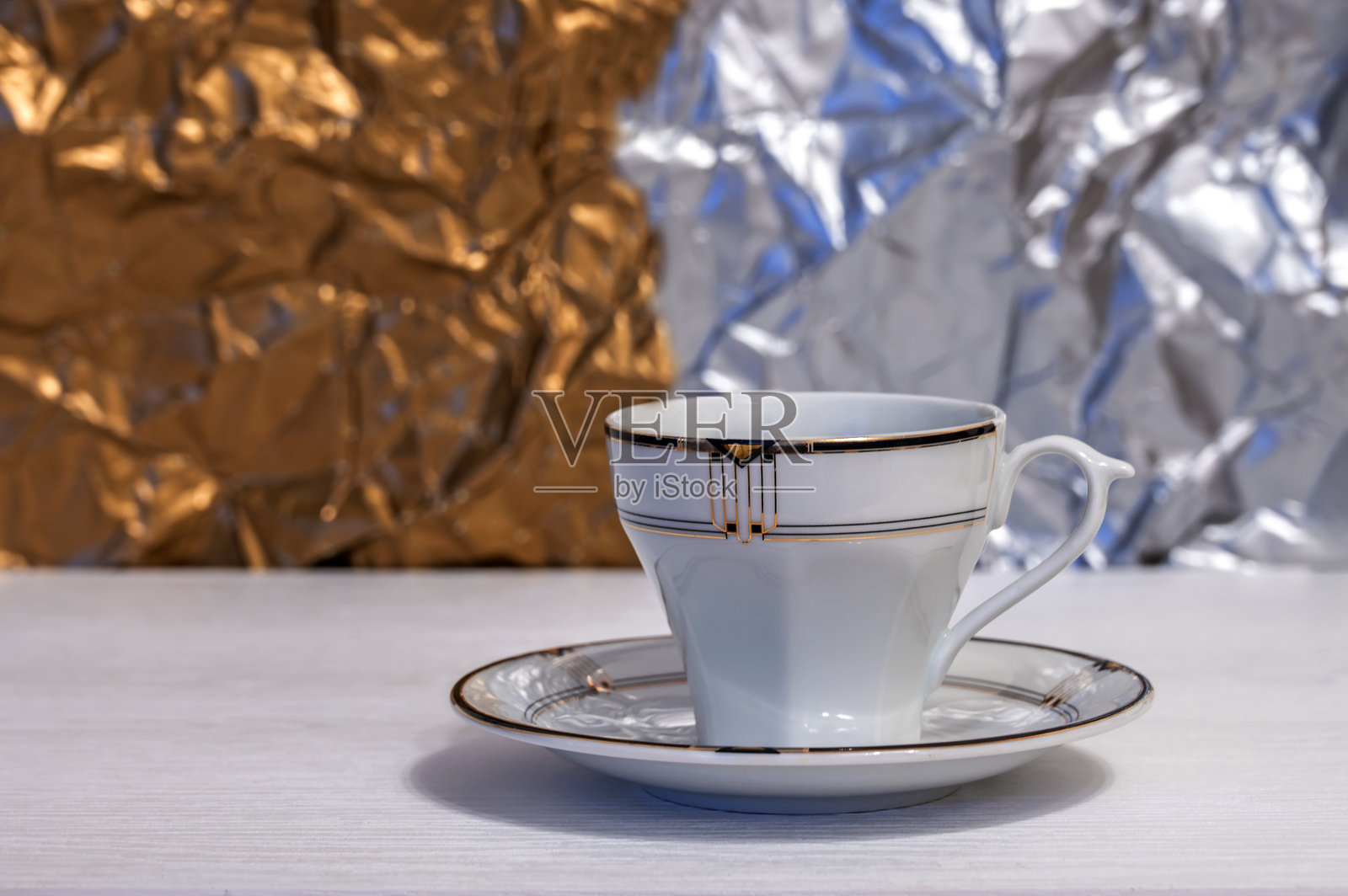 空白的白色杯子和碟子放在白色桌子上，背景是银色和金色。照片摄影图片