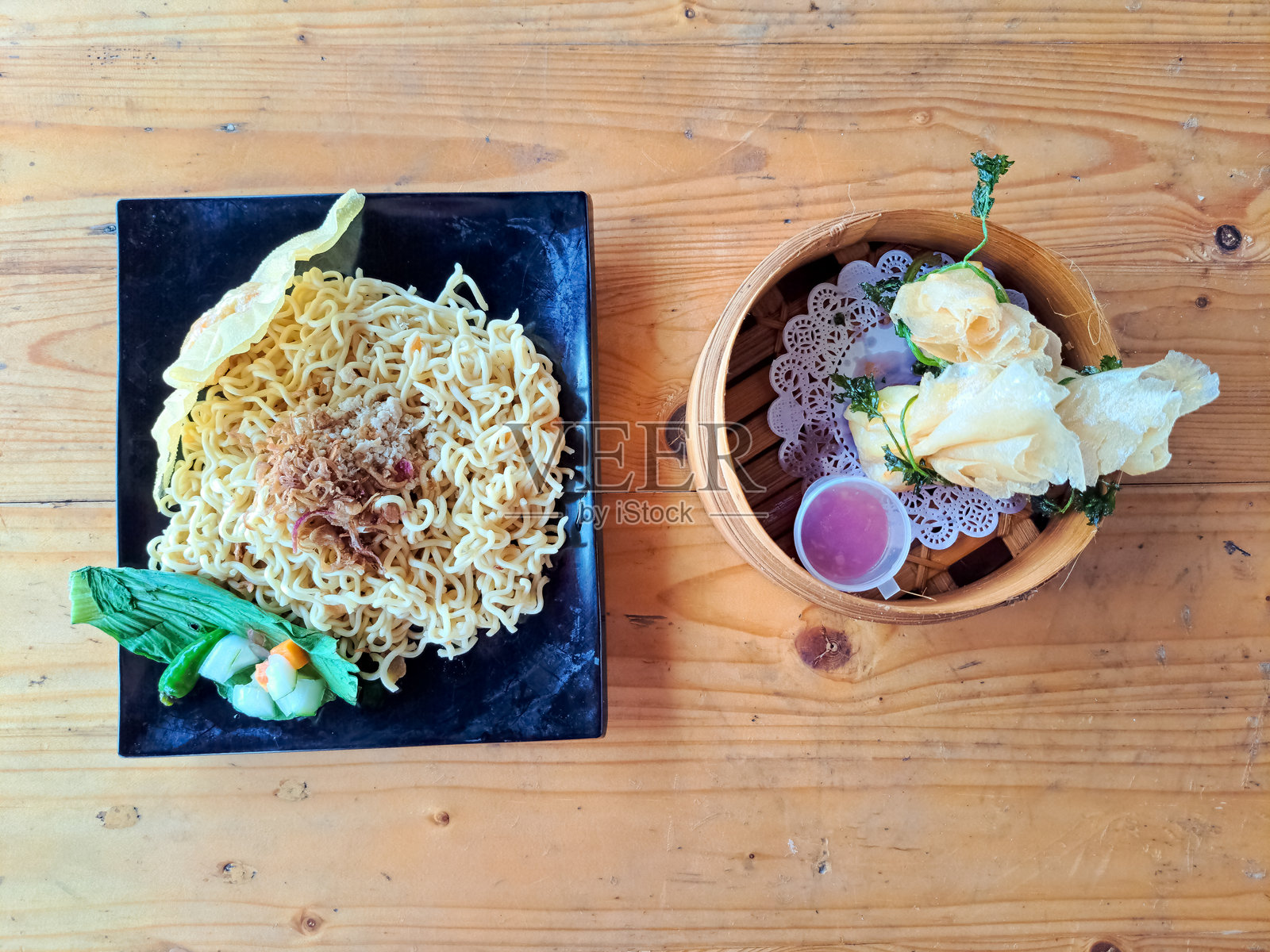 美味的炒米粉或炒面，配有炸饺子、鸡肉撒料、炸洋葱、青芥菜、黄瓜和胡萝卜，摆放在盘子上。碗中盛有炸鱼饼。食品菜单。俯视图。照片摄影图片