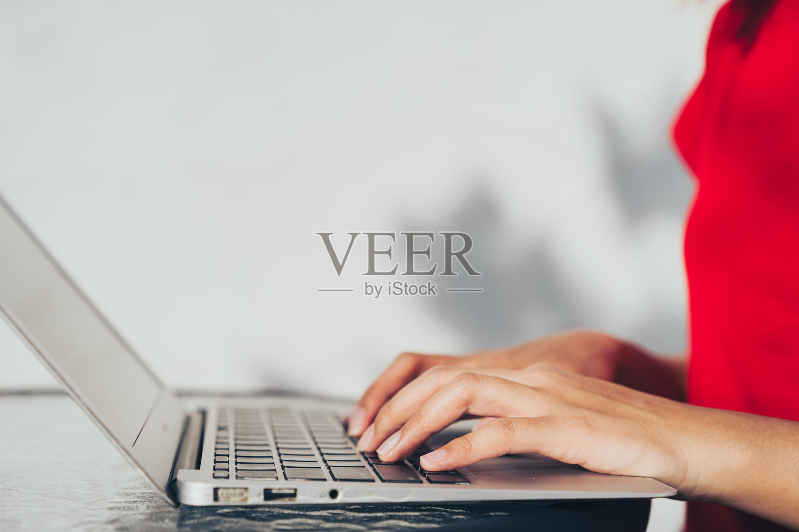 穿着红色衬衫的人在笔记本电脑上打字，专注于工作。背景柔和模糊，营造出宁静的工作氛围。照片摄影图片