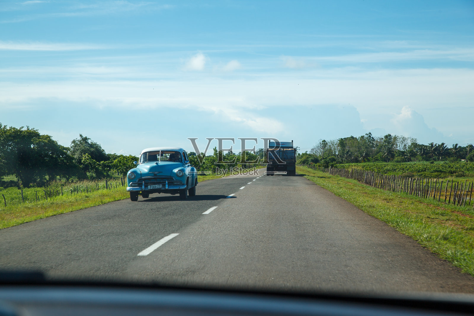 在古巴的乡村道路上，一辆复古蓝色汽车与一辆卡车交错，位于哈瓦那和西恩富戈斯之间。照片摄影图片