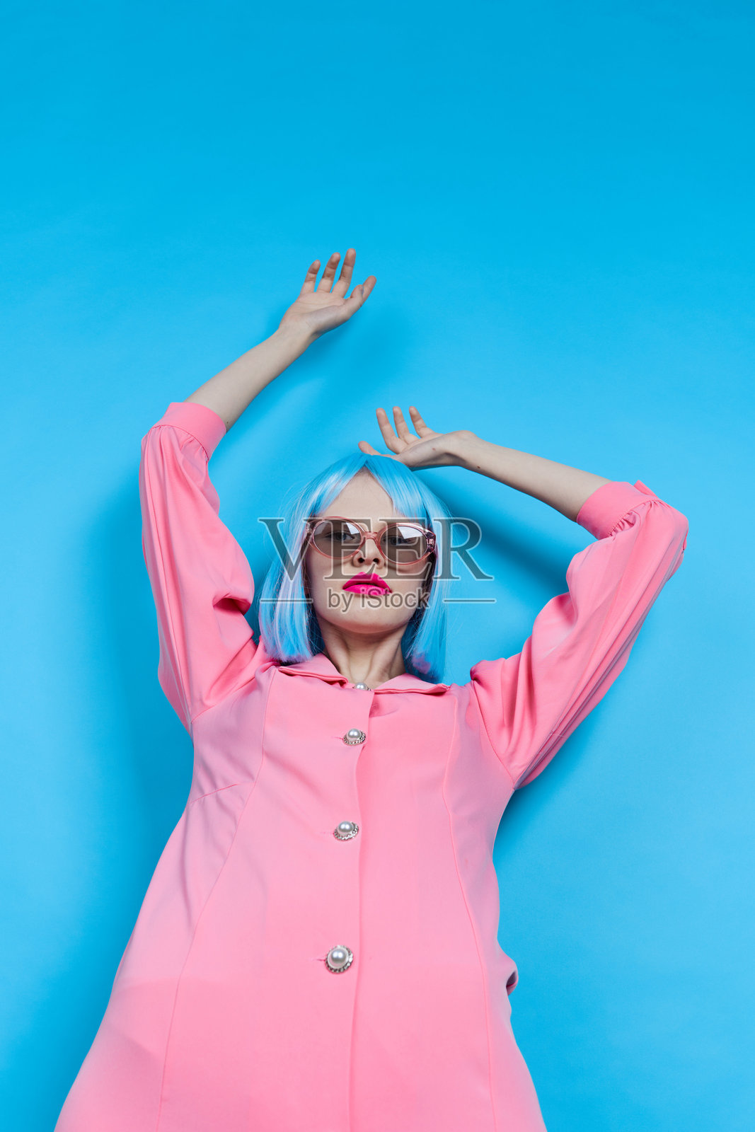 戴着太阳镜的女性肖像，穿着蓝色假发，化妆，背景为单色。照片摄影图片