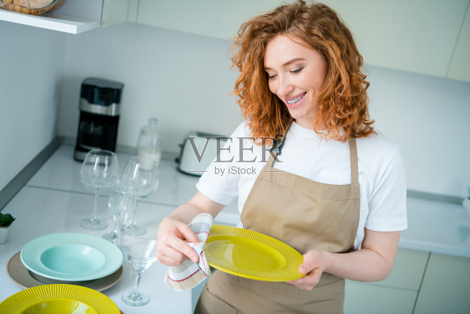年轻女子在休闲的厨房环境中，穿着围裙，面带灿烂笑容，正在准备美食，享受阳光明媚的室内时光。照片摄影图片