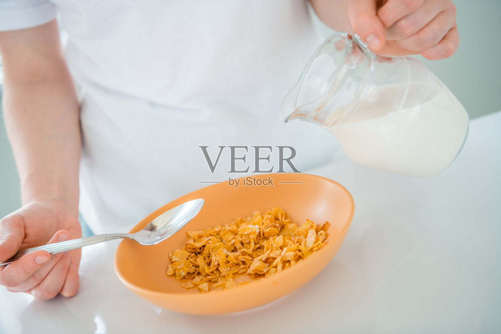 年轻女性穿着休闲风格，在明亮的厨房里享受早餐，同时将新鲜牛奶倒在酥脆的麦片上。照片摄影图片
