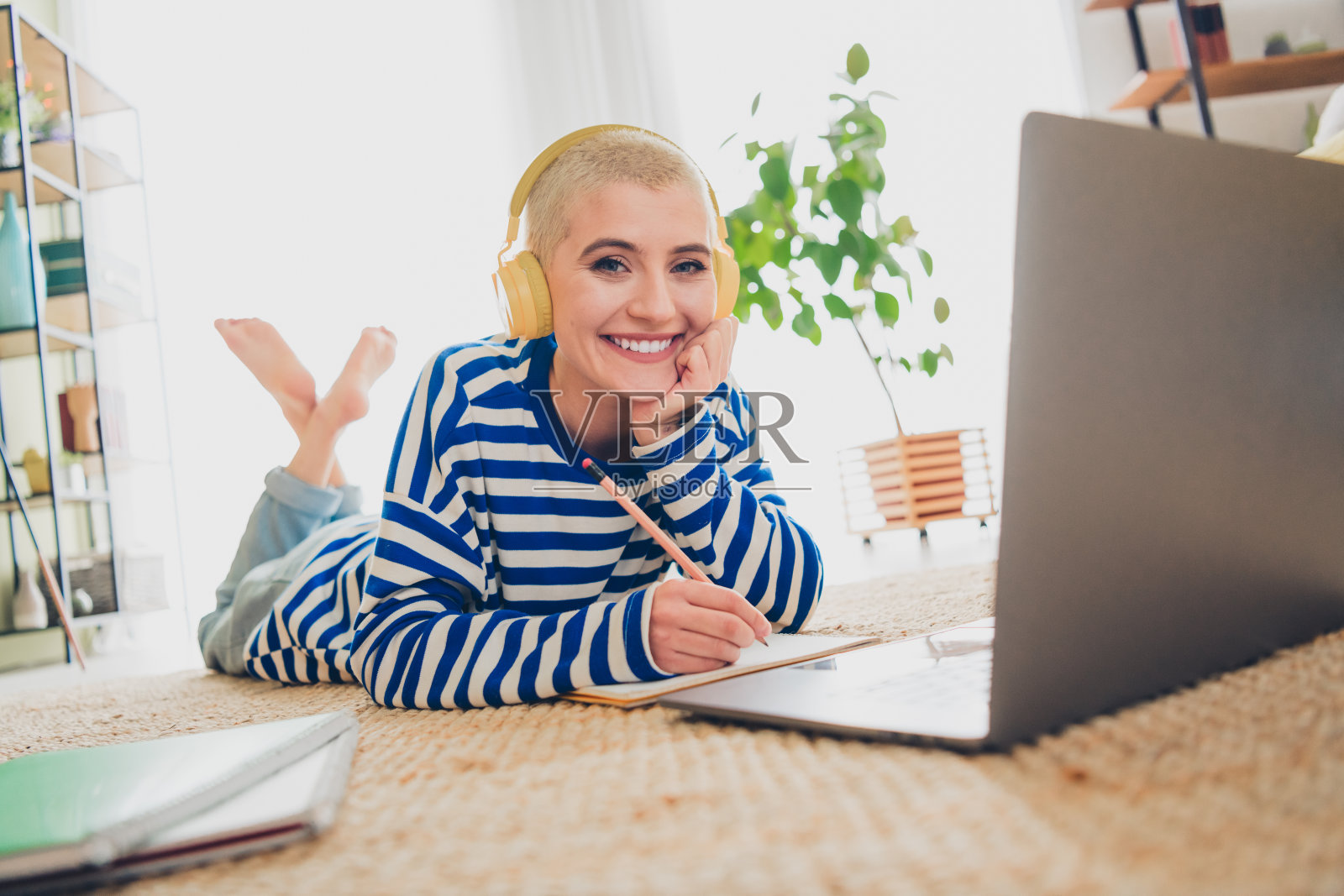 年轻女性在舒适的客厅里放松，穿着条纹毛衣，微笑着戴着耳机，享受休闲活动。照片摄影图片