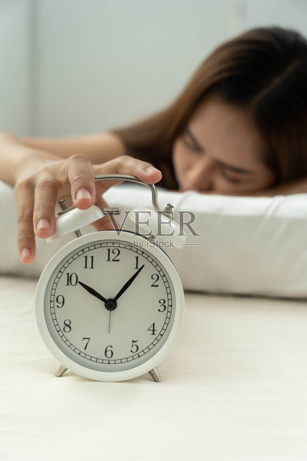 懒惰的亚洲年轻女性关掉闹钟，女士迟到了约会、工作或上课，睡过头，早上起床困难，时间紧迫，没能准时，困倦，过期，快点，时间不够。照片摄影图片