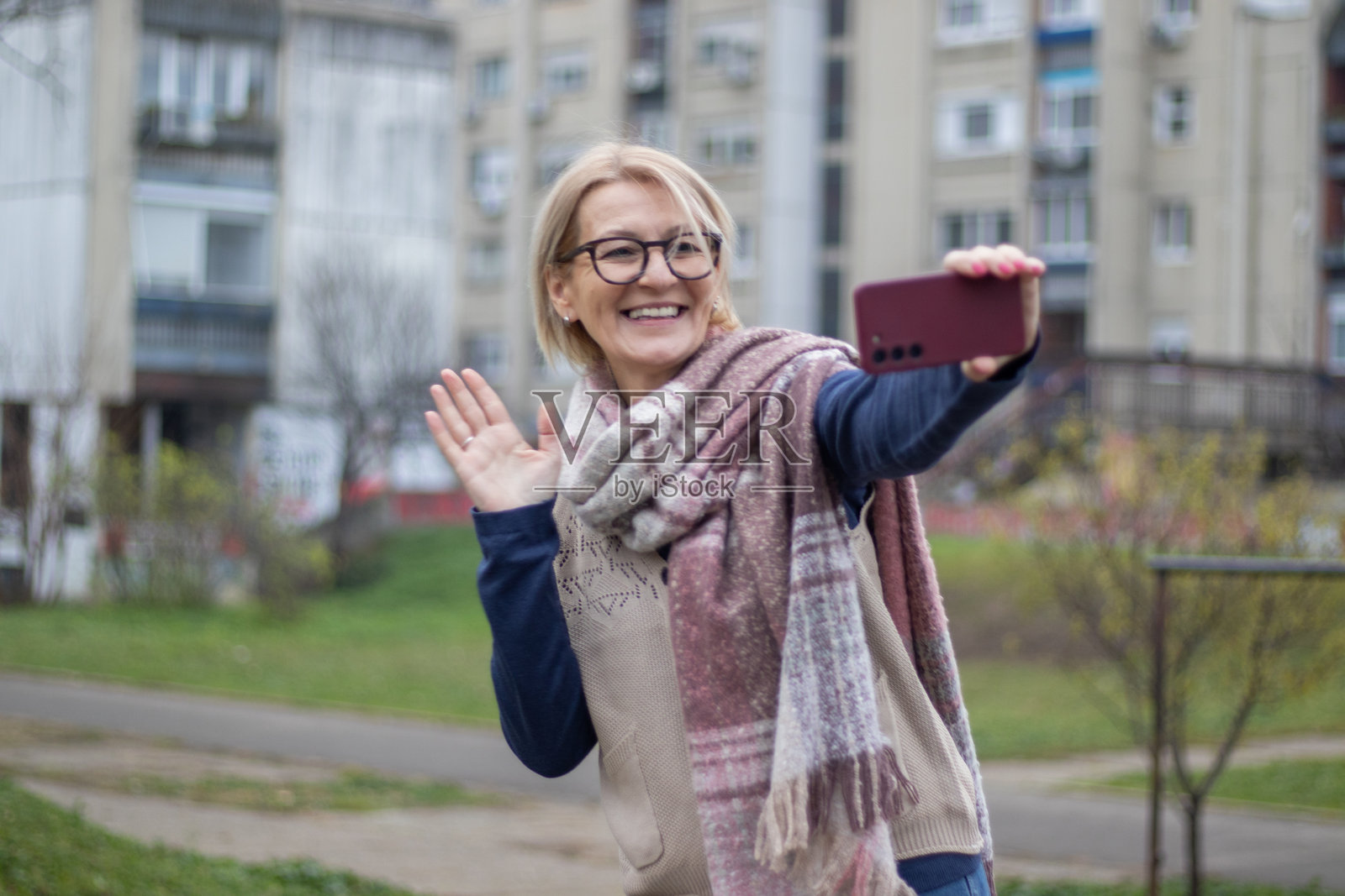 一位成熟的金发女性在冬日的城市公园里戴着眼镜，面带微笑自拍。照片摄影图片