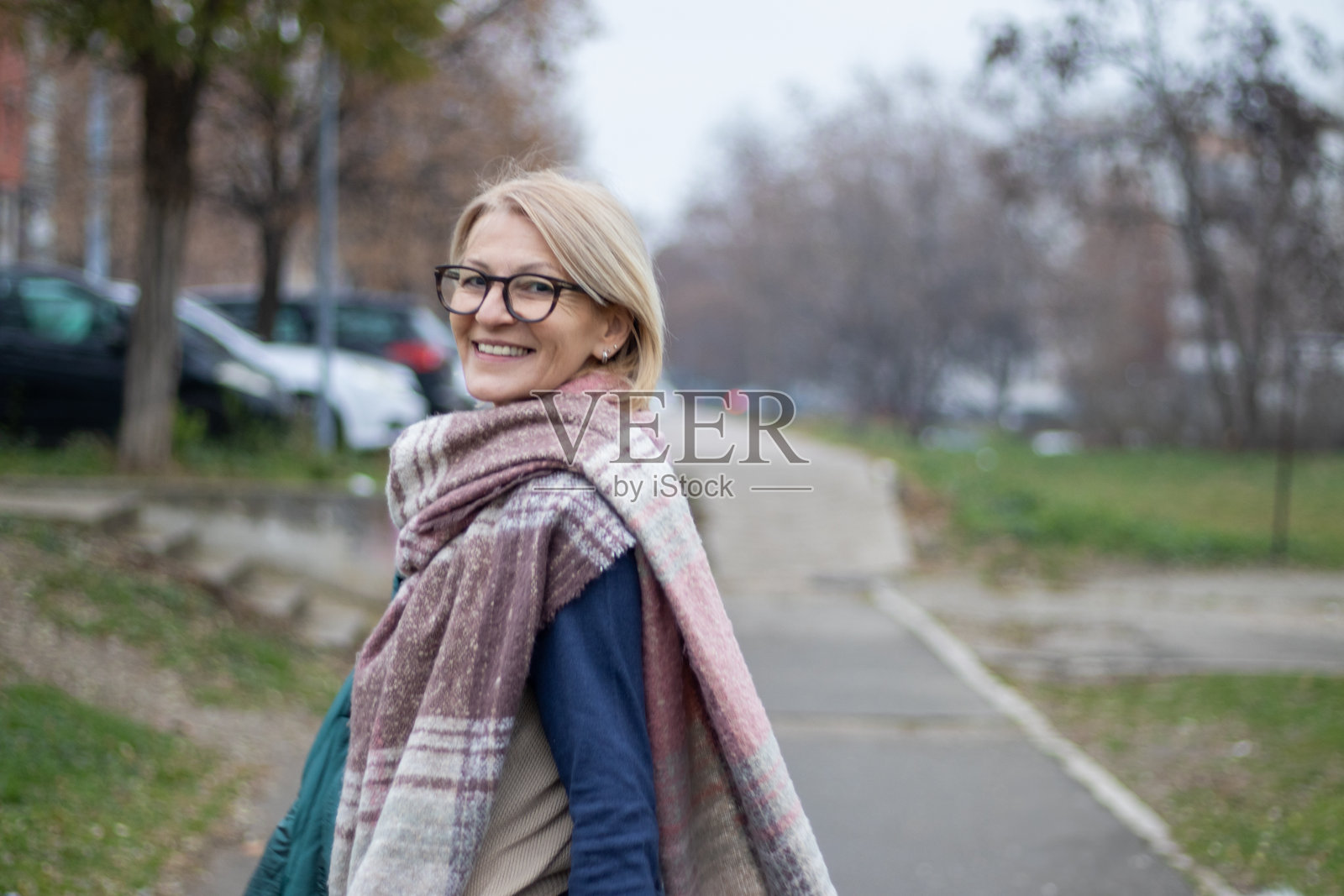 冬日的城市公园里，一位成熟的金发女性戴着眼镜，微笑着愉快地看向镜头。照片摄影图片