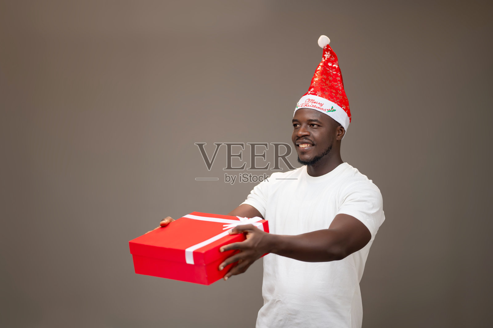 年轻的非裔美国男性微笑着戴着圣诞帽，手里拿着一个礼物盒。照片摄影图片