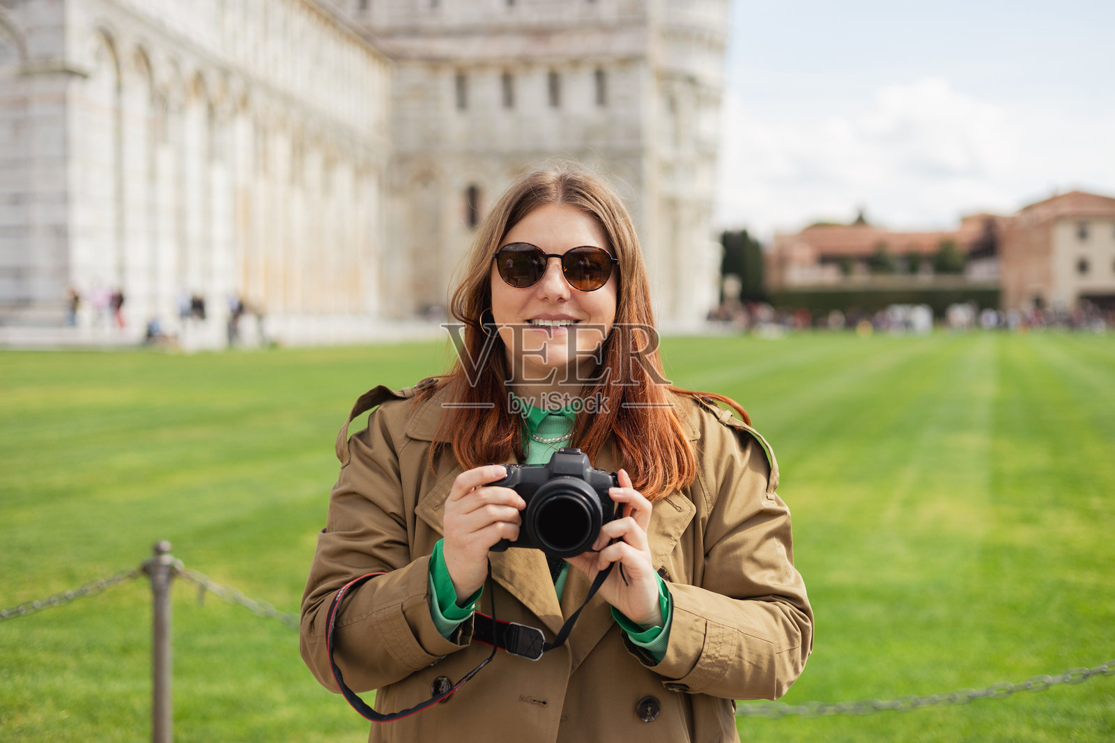 快乐的30多岁女性摄影师在户外用相机拍照。女性游客在阳光明媚的城市中使用数码相机。照片摄影图片