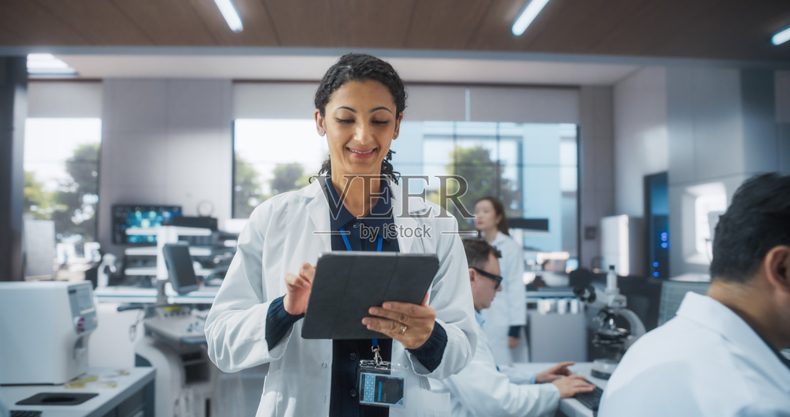 印度女性手持平板电脑，浏览研究数据。一组多元化的男女医学研究科学家在现代实验室中研发新一代医疗产品。照片摄影图片