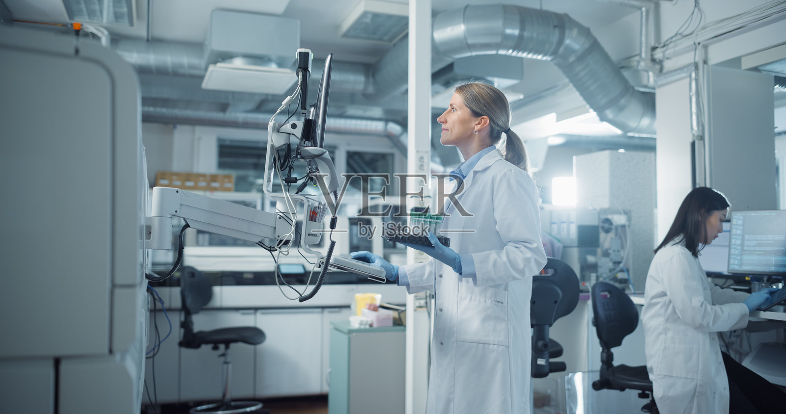 穿着白色实验室外套的科学家在现代实验室中操作先进的测试设备。处理样本并在电脑上分析数据。研究人员与同事在高科技环境中合作。照片摄影图片