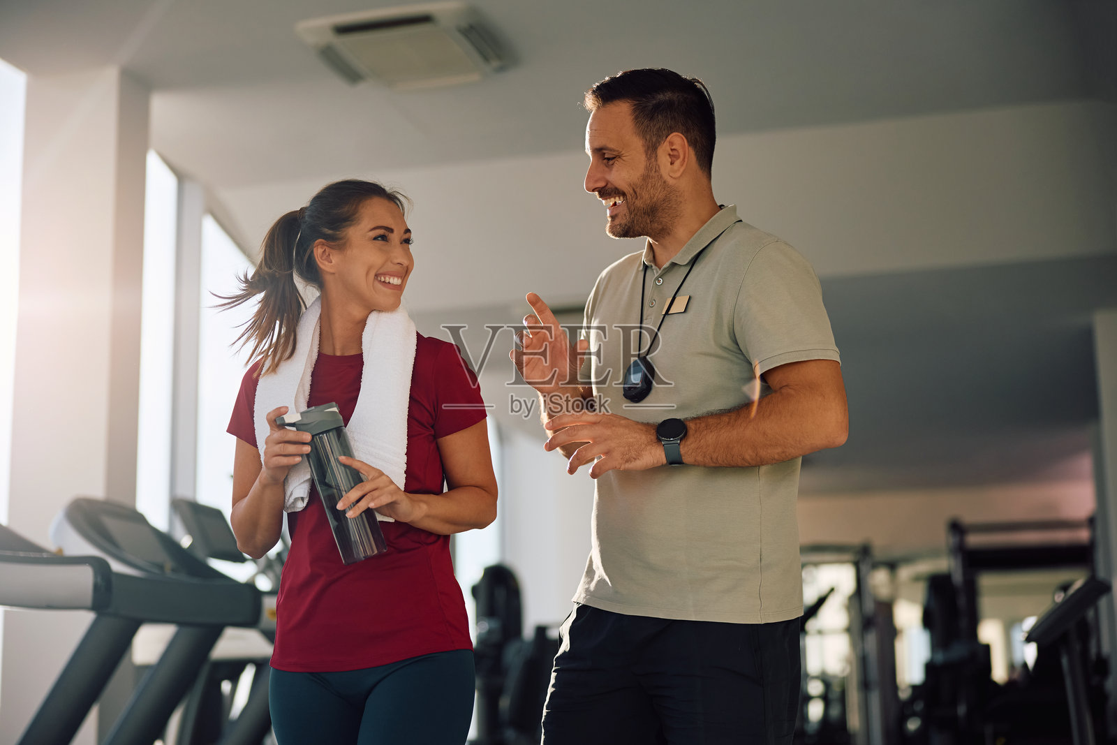 快乐的运动女性在健身房锻炼时与她的私人教练交谈。照片摄影图片