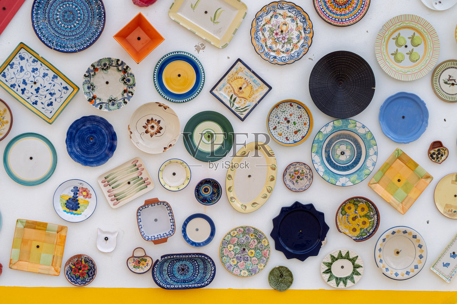 五彩缤纷的陶瓷盘子和碗挂在白色墙壁上，形成生动的展示照片摄影图片