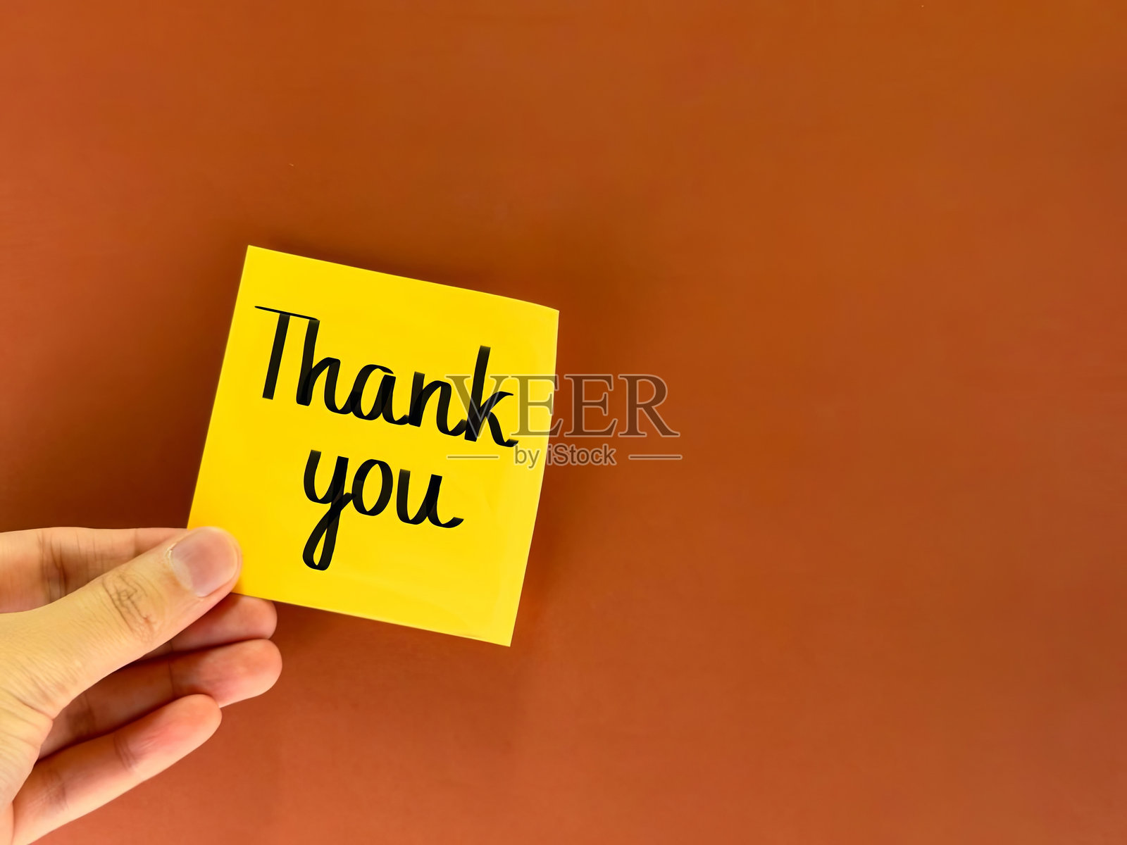 办公室纸上的感谢字样。手中递出一张写有感谢的纸。感谢信。一张带有感谢字样的贴纸，背景为纸质。照片摄影图片
