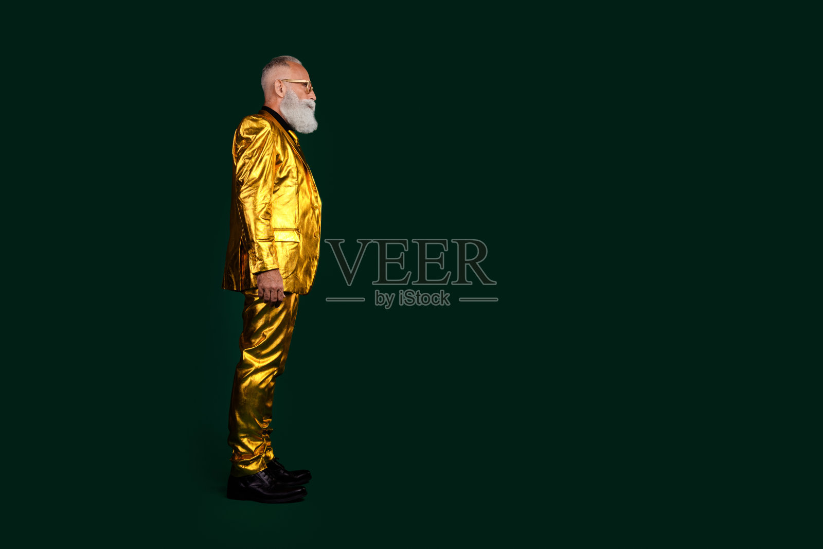优雅的老年绅士身穿闪亮的金色西装，自信地站在深绿色背景前。照片摄影图片
