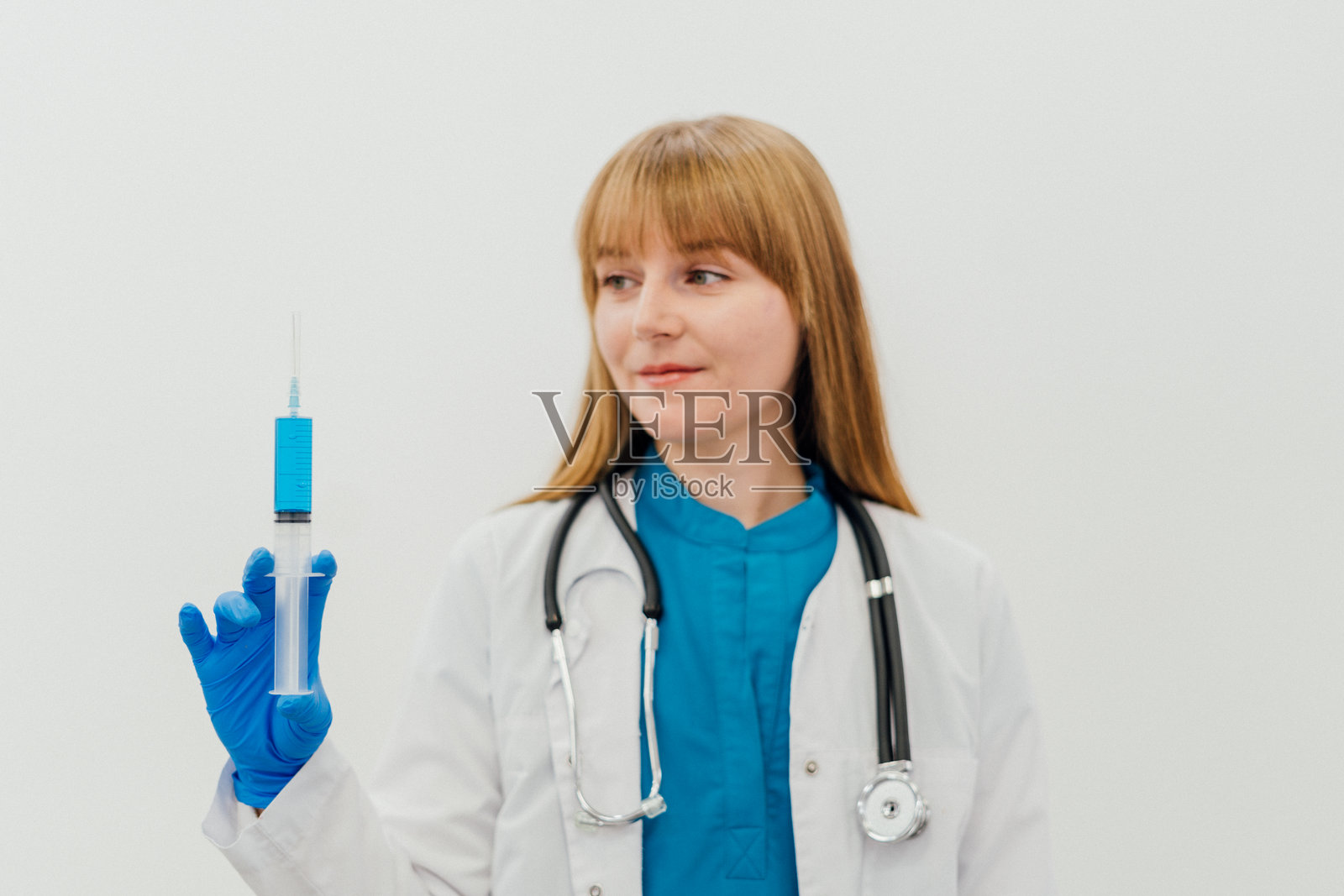 一位穿着白大褂和蓝色手套的女性医生手持装有蓝色液体的注射器。专业的医疗工作者在临床环境中，象征着精准、安全和医疗护理。照片摄影图片