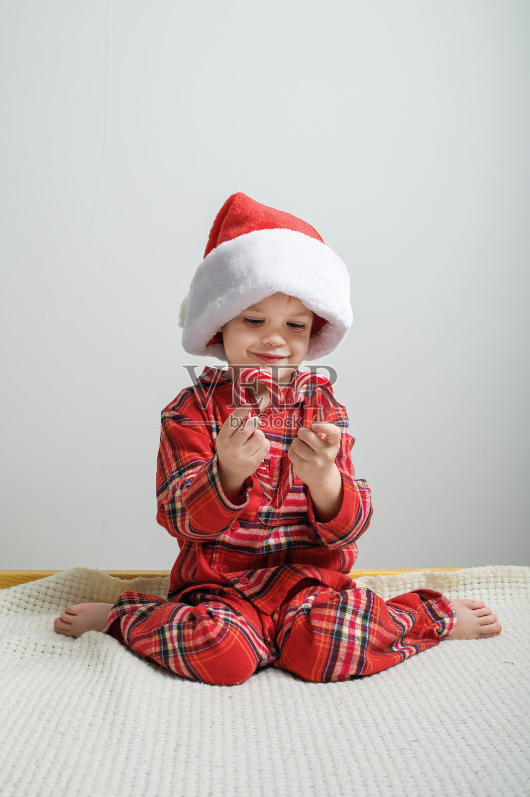 可爱的孩子戴着圣诞老人帽，手里拿着糖果手杖。照片摄影图片