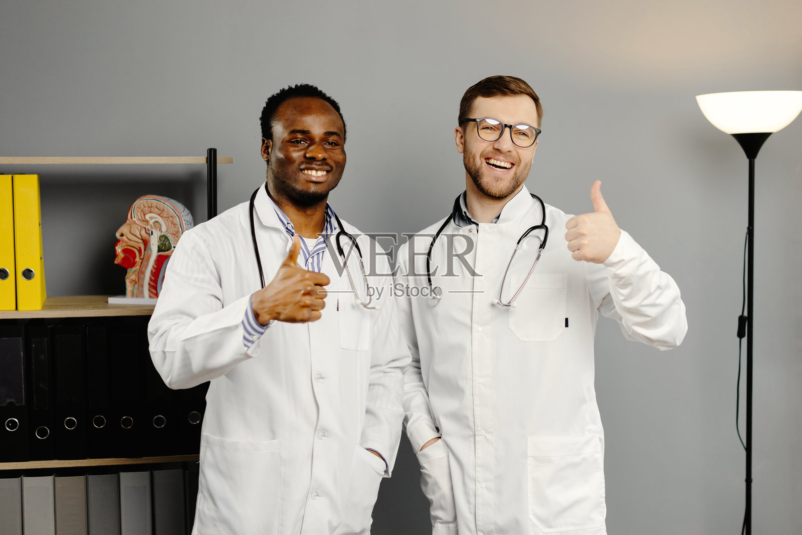 两名穿着白色实验室外套的男子站在桌子旁边。照片摄影图片