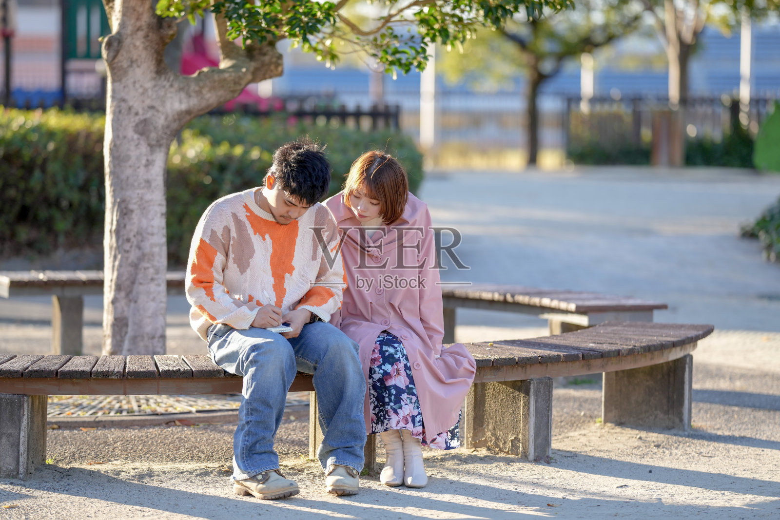 一对二十多岁的情侣坐在长椅上，在爱知县半田市的大公园里交谈，正值秋季。照片摄影图片