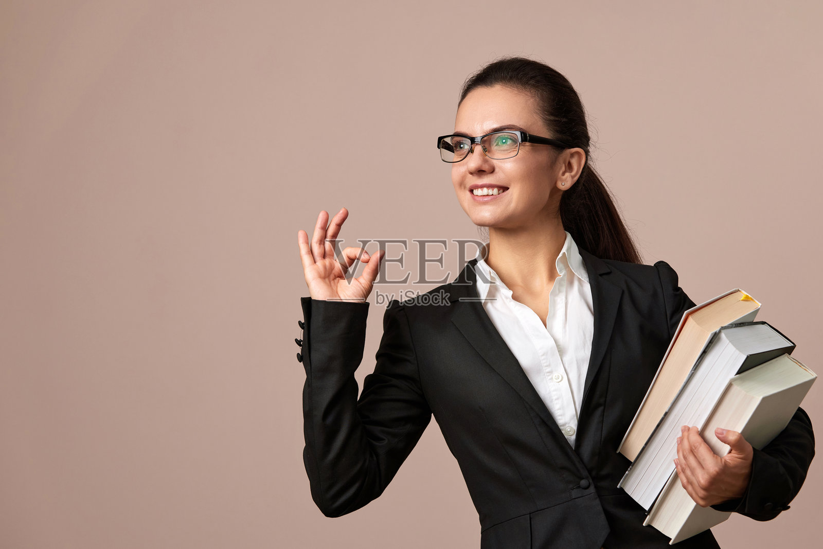 戴眼镜的迷人女性穿着黑色夹克，手里拿着一叠书。照片摄影图片