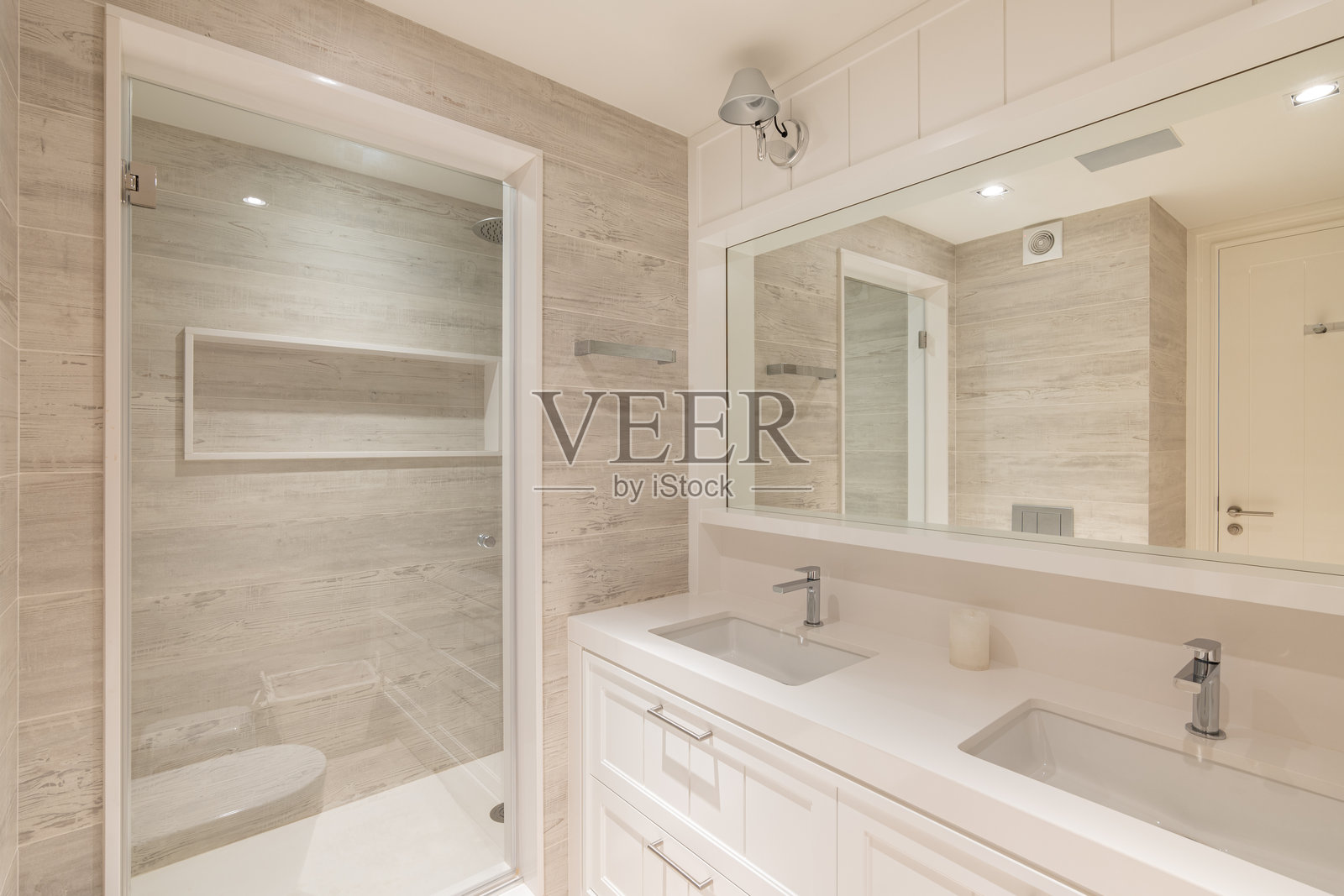 现代公寓内的浴室，配有米色瓷砖、透明淋浴门和两个洗手盆。照片摄影图片