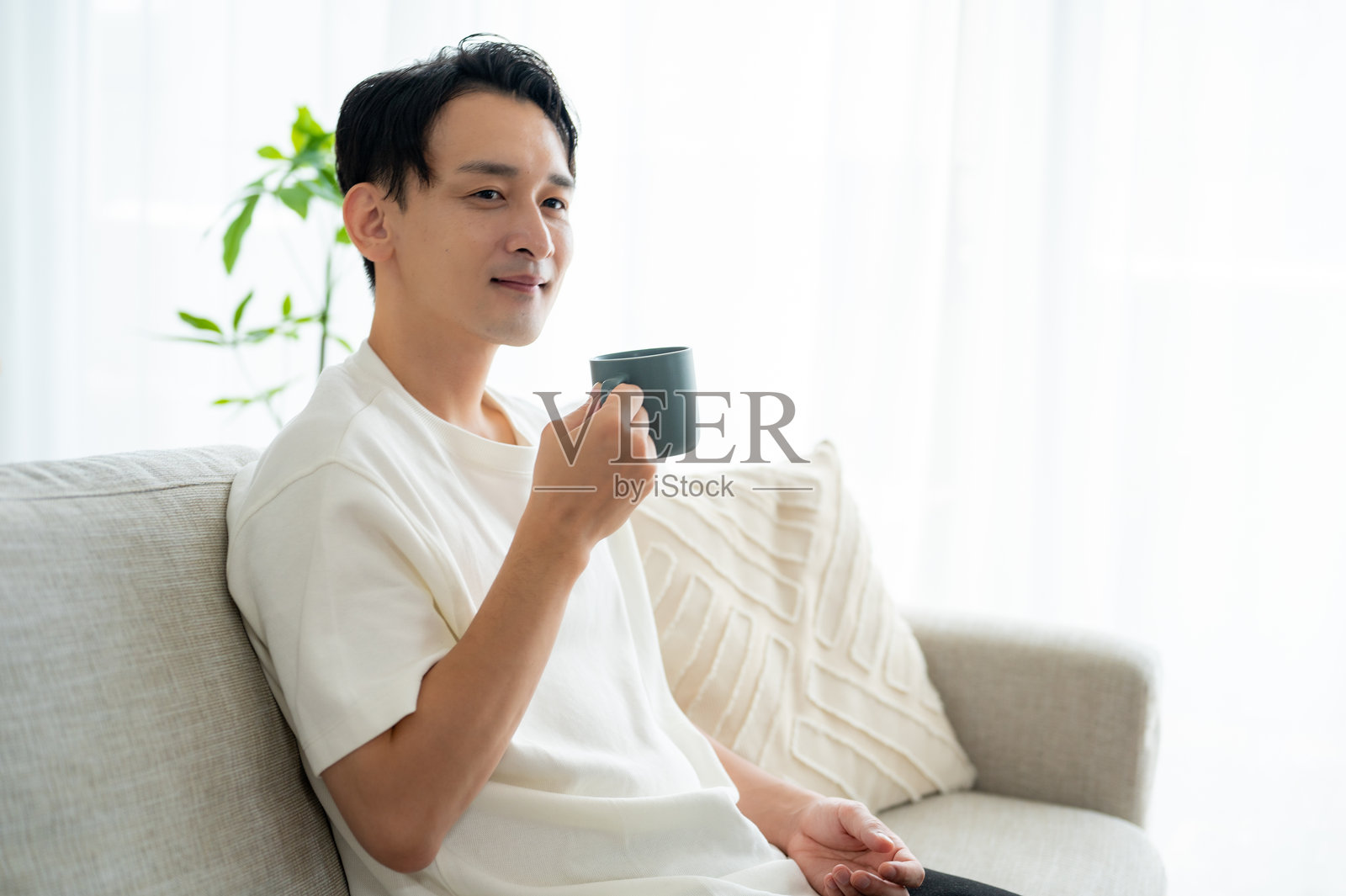 一个男人坐在沙发上，手里拿着一个杯子照片摄影图片