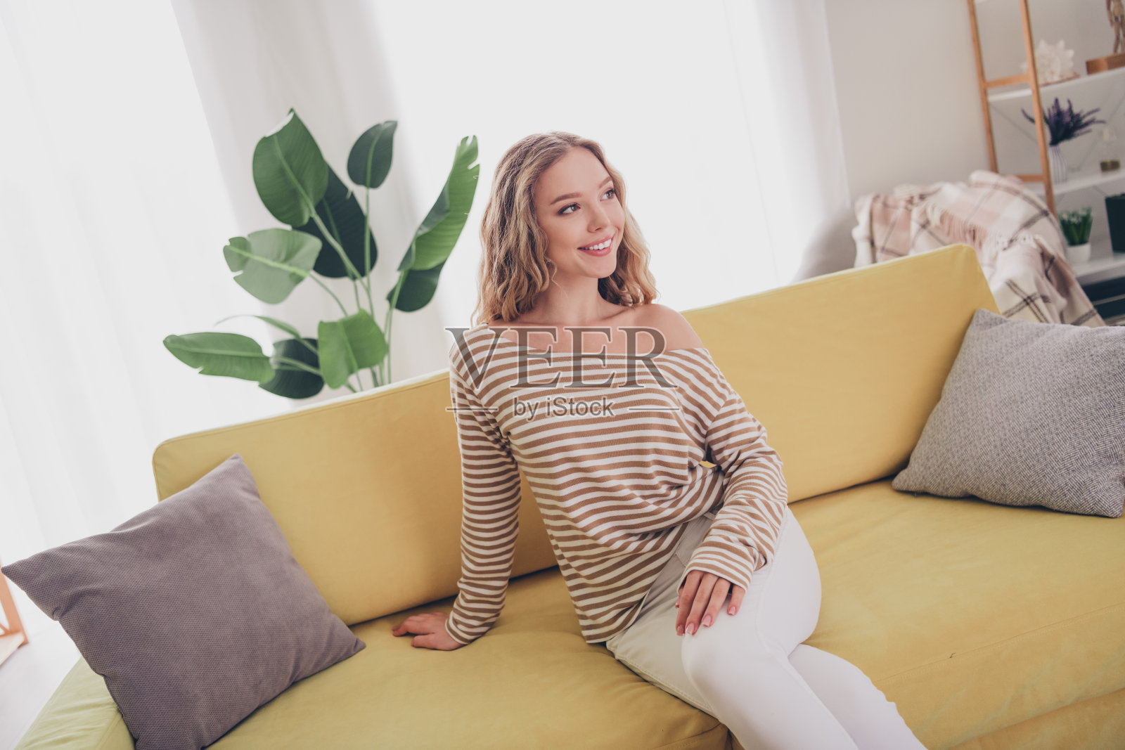 年轻女性穿着休闲条纹毛衣，在舒适的客厅享受轻松的周末，沐浴在阳光和积极的氛围中。照片摄影图片