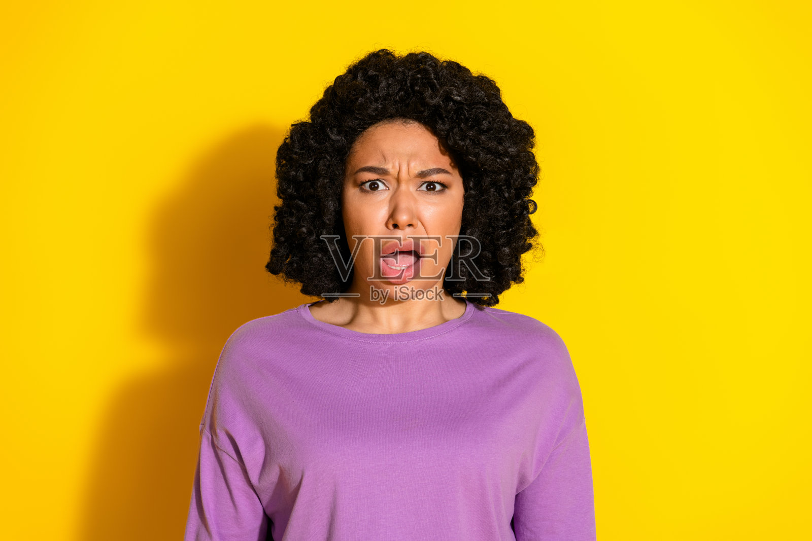 漂亮年轻女孩张嘴凝视，穿着紫色毛衣，背景为黄色。照片摄影图片
