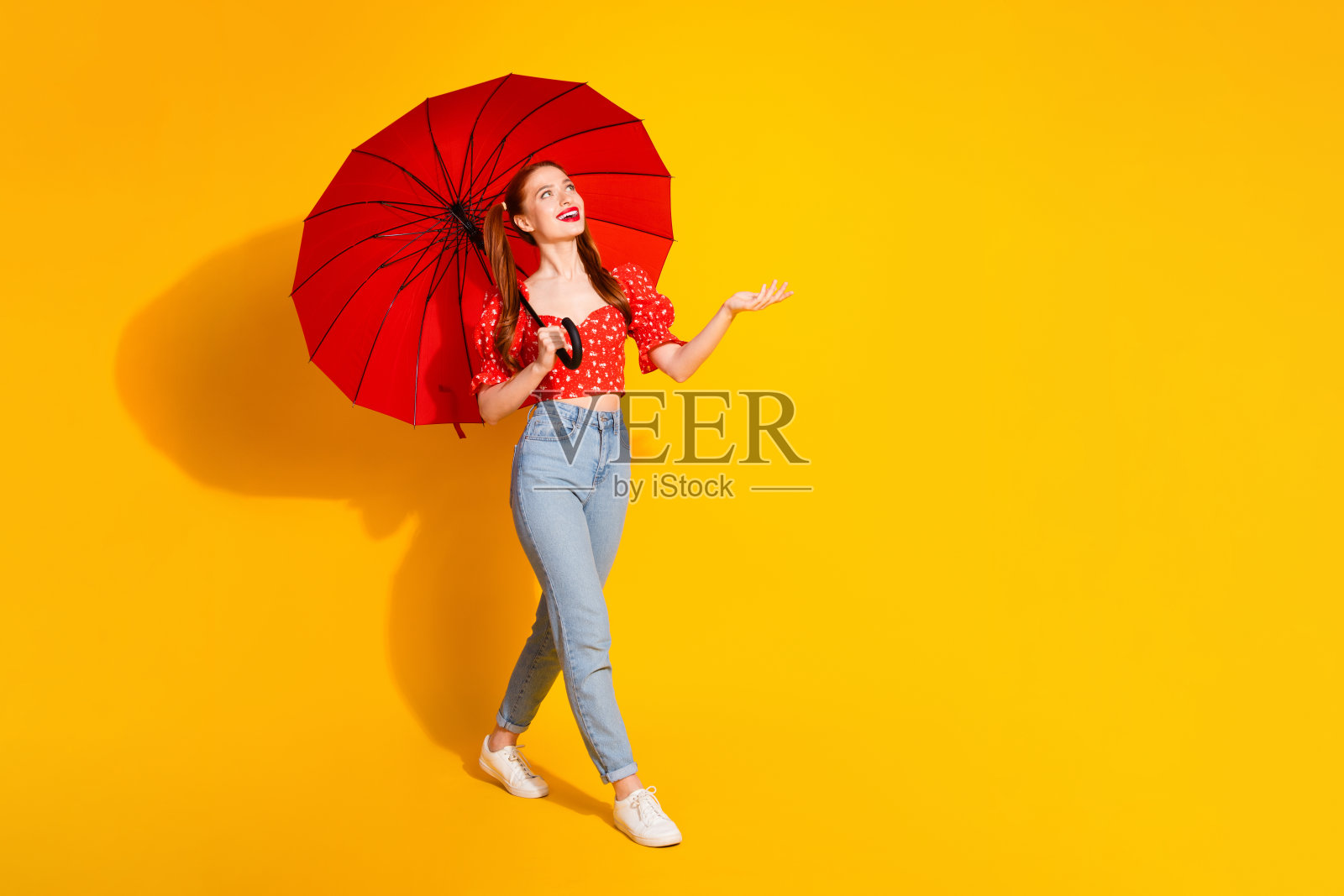 年轻漂亮的女孩穿着红色上衣和牛仔裤，手持雨伞在黄色背景下走动，捕捉雨滴。照片摄影图片