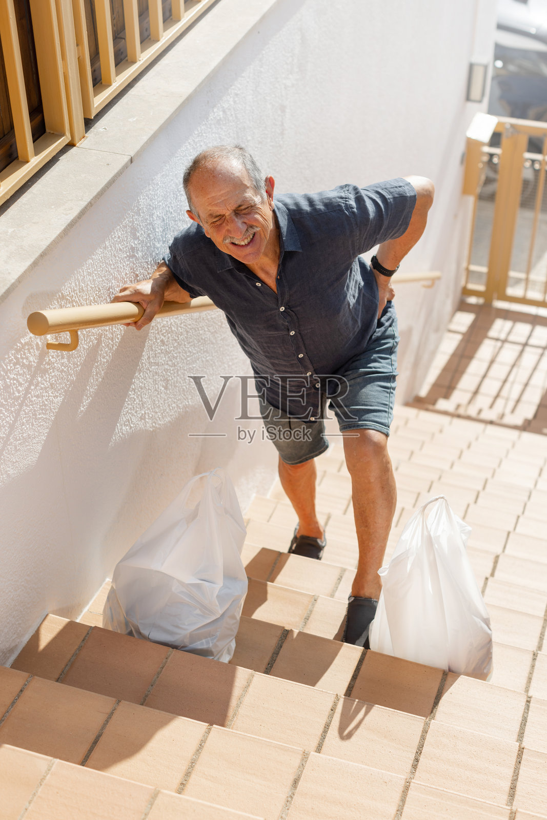 一位老年男子向前倾身，因爬楼梯后背部疼痛而扶着自己的背部。照片摄影图片