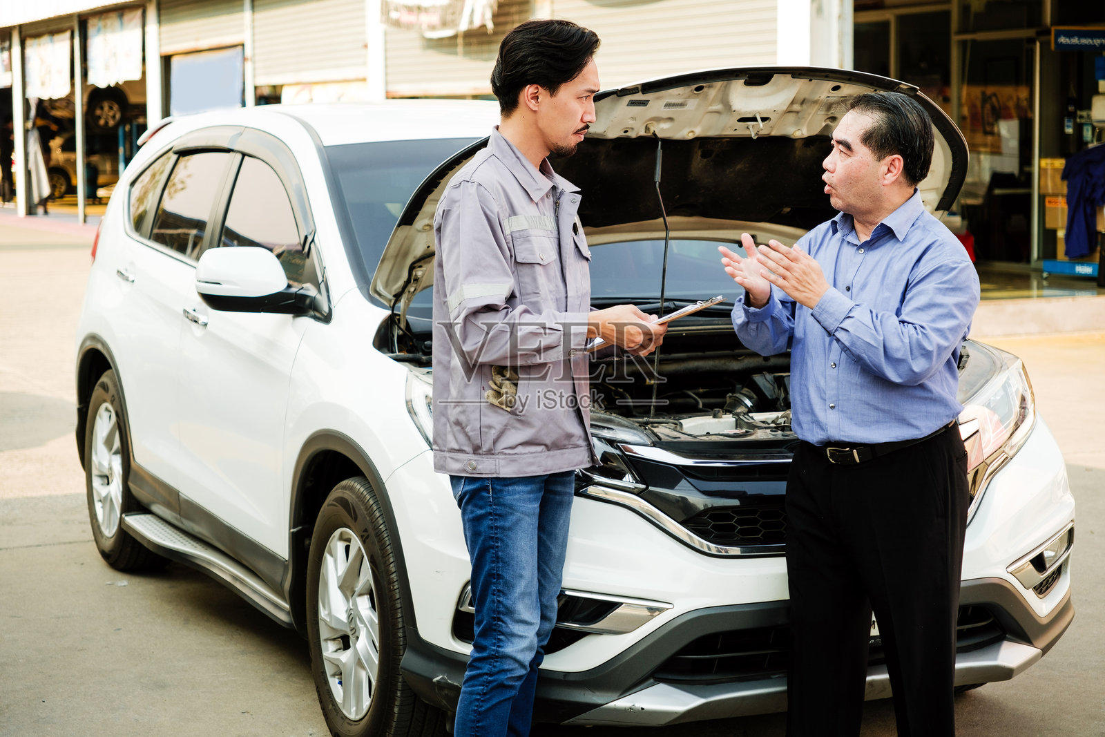 日本机械师为亚洲客户检查汽车的清单，车前盖打开，专注于右侧的机械师和客户。汽车维修服务中心，专业服务。照片摄影图片