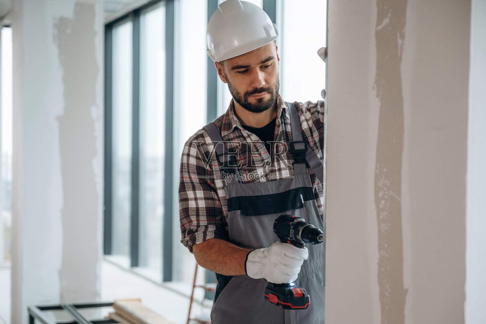 在墙上钻孔。一名男子正在翻新一个未完成的房间。照片摄影图片